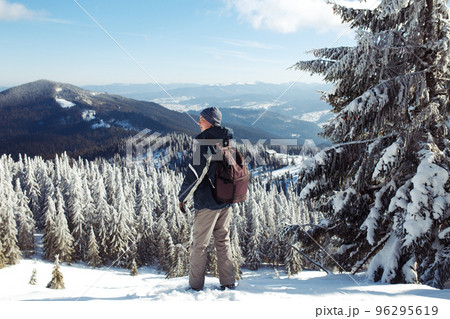Man with backpack trekking in mountains. Cold weather, snow on hills. Winter hiking. 96295619