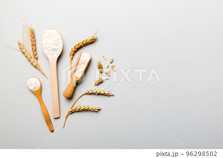 Flat lay of Wheat flour in wooden bowl with wheat spikelets on colored background. world wheat crisis Flat lay of Wheat flour in wooden bowl with wheat spikelets on colored background. world wheat crisis 96298502