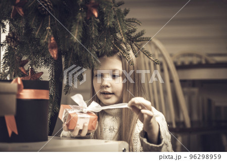 Merry Christmas, happy holidays. Cheerful cute little blonde girl opens a Christmas present 96298959