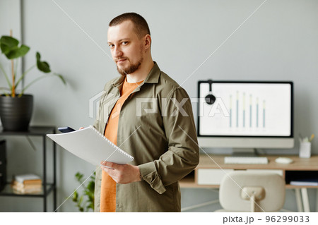 Man standing in minimal office and holding document 96299033