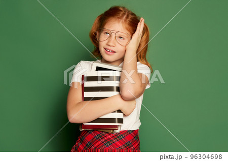 Student or pupil of elementary school wearing modern school uniform posing isolated over dark green background. Happy charming girl, kid with books 96304698