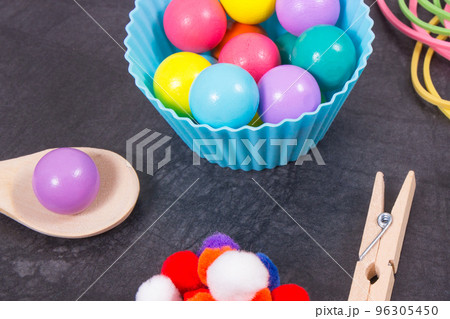 Colorful pompoms, balls and rubber erasers with spoon and tongs. Development of kids motor skills Colorful pompoms, balls and rubber erasers with spoon and tongs. Development of kids motor skills 96305450