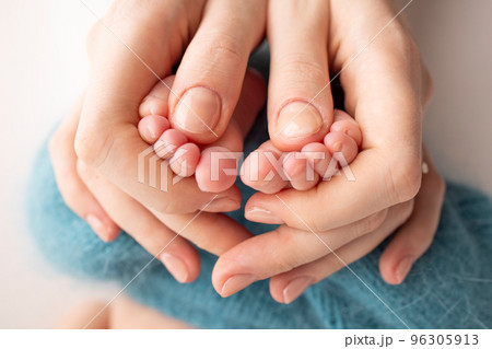 Mother is doing massage on her baby foot. Close up baby feet in mother hands on a blue background. Prevention of flat feet, development, muscle tone, dysplasia. Family, love, care, and health concept 96305913