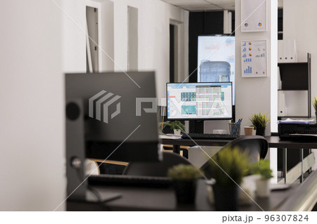 Workstations with desktop devices on wooden desks in contemporary coworking office. Empty workspace before staff arrives to work early in the morning, indoor working concept. 96307824