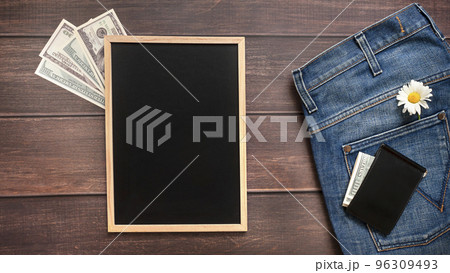 Men's Blue Jeans with Daisy flower in the pocket  and Wallet on Brown background with chalkboard with place for text. Holidays and buying presents concept. Men's Blue Jeans with Daisy flower in the pocket  and Wallet on Brown background with chalkboard with place for text. Holidays and buying presents concept. 96309493