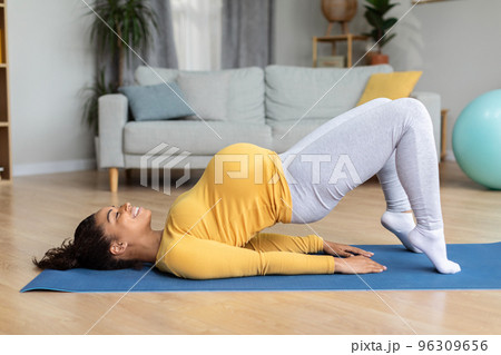 Satisfied young black pregnant woman with big belly practicing yoga on mat, enjoy workout 96309656