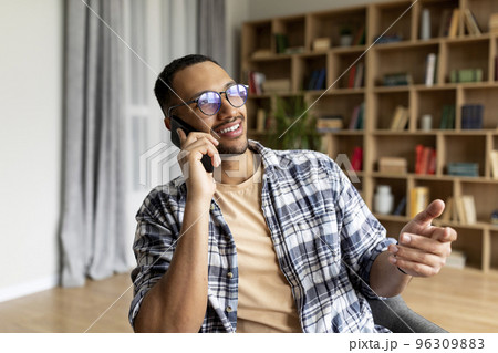 Happy arab man talking on smartphone and smiling while resting in armchair in living room interior, free space 96309883