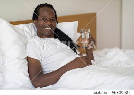Handsome African American Guy Holding Glass With Water While Relaxing In Bed 96309985