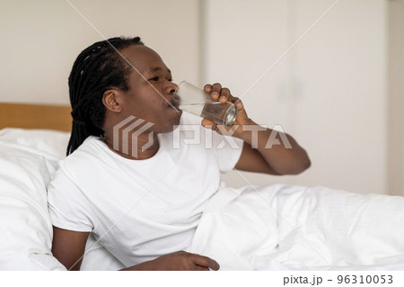Thirsty Black Man Drinking Water From Glass While Resting In Bed Thirsty Black Man Drinking Water From Glass While Resting In Bed 96310053