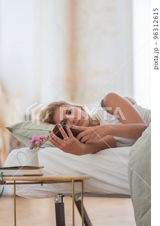 Focused woman lying in bed in morning and looking at phone screen Focused woman lying in bed in morning and looking at phone screen 96312615
