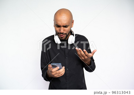 Portrait of indignant young man in headphones using mobile phone Portrait of indignant young man in headphones using mobile phone 96313043