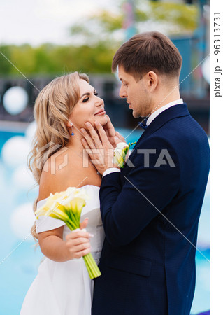 bride and groom in classic clothes by the pool decorated with white balloons.  96313731