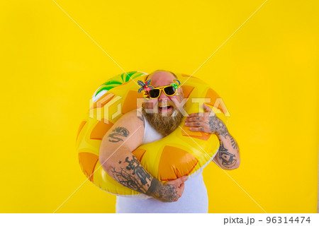 Fat happy man with wig in head is ready to swim with a donut lifesaver Fat happy man with wig in head is ready to swim with a donut lifesaver 96314474