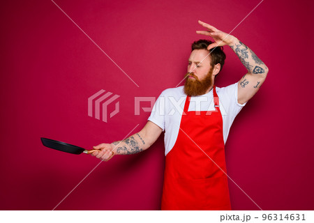 serious chef with beard and red apron cooks with pan 96314631