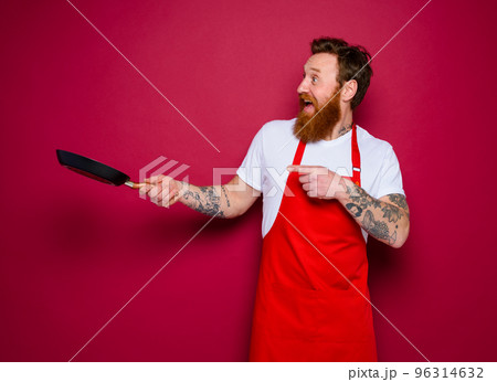 amazed chef with beard and red apron cooks with pan 96314632