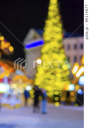 Blurred background. Christmas tree, decorated glowing lights, building, blurry silhouettes of people walking city square at winter night. Beautiful New Year and Christmas holiday blurred background Blurred background. Christmas tree, decorated glowing lights, building, blurry silhouettes of people walking city square at winter night. Beautiful New Year and Christmas holiday blurred background 96314677