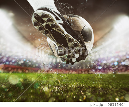 Football scene at night match with close up of a soccer shoe hitting the ball with power Football scene at night match with close up of a soccer shoe hitting the ball with power 96315404