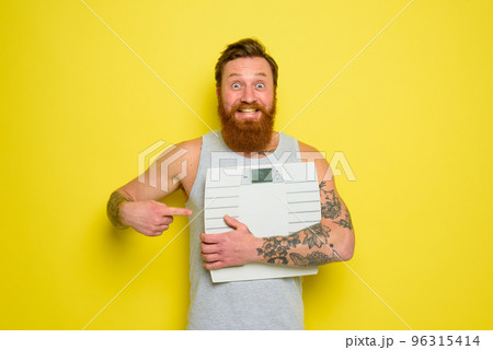 Amazed man with beard and tattoos holds an electronic balance Amazed man with beard and tattoos holds an electronic balance 96315414