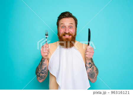 Happy man with tattoos is ready to eat with cutlery in hand Happy man with tattoos is ready to eat with cutlery in hand 96316121