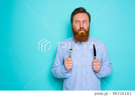 Man with tattoos is ready to eat with cutlery in hand 96316161