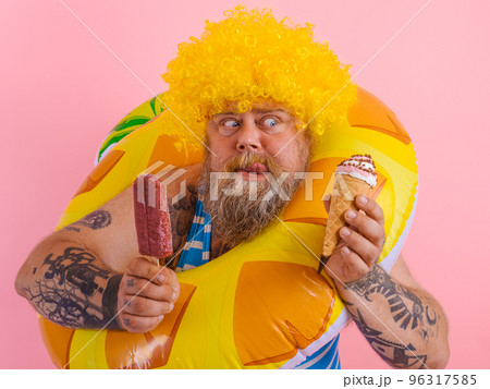 Fat man with beard and wig eats a popsicle and an icecream Fat man with beard and wig eats a popsicle and an icecream 96317585