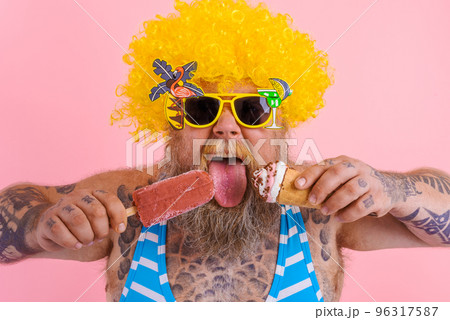 Fat man with beard and wig eats a popsicle and an icecream 96317587