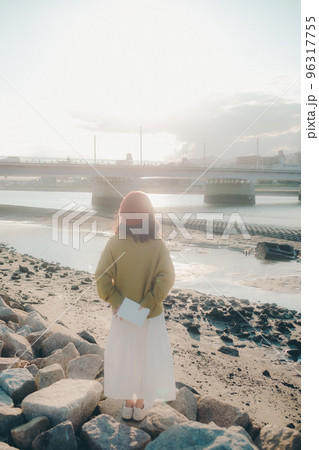 河川敷で読書をしながら佇む若い女性の写真 河川敷で読書をしながら佇む若い女性の写真 96317755