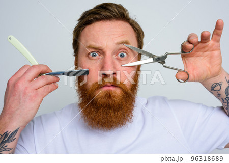Worried man with scissors and blade is ready to cut the beard Worried man with scissors and blade is ready to cut the beard 96318689
