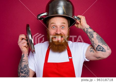 Happy chef with beard and red apron plays with pot 96318718