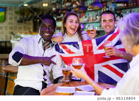 Glad males and females with UK flag clinking glasses with beer on party Glad males and females with UK flag clinking glasses with beer on party 96319804