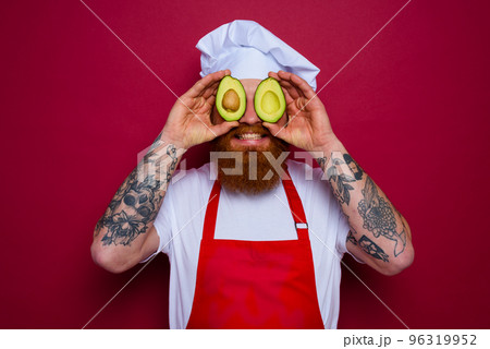 happy chef with beard and red apron holds an avocado 96319952
