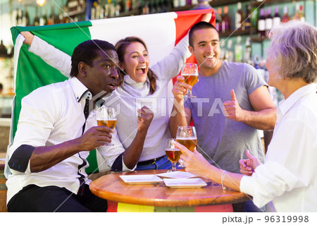 Excited diverse soccer supporters with flag of Italy celebrating victory with pint of beer in the pub 96319998
