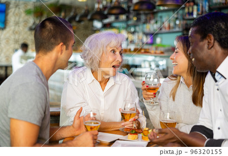 Cheerful international friends different ages enjoying pinchos and beer in the evening pub Cheerful international friends different ages enjoying pinchos and beer in the evening pub 96320155