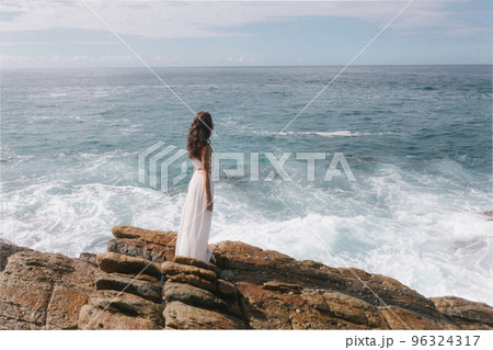 Aerial drone view of bride in an amazing dress standing on a cliff and looking at the sea 96324317