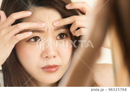 鏡で眉間のしわを見る女性。 96325768