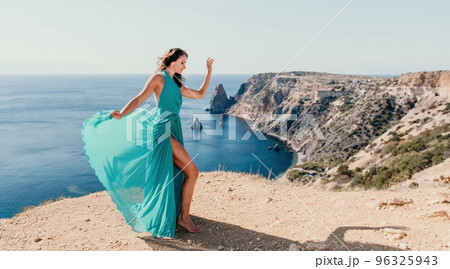 Side view a Young beautiful sensual woman with black hair in a long mint dress posing on a beach with calm sea bokeh lights on sunny day. Girl on the nature on blue sky background. Fashion photo 96325943