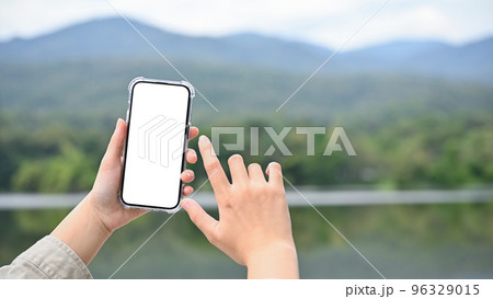 Young Asian female using her modern smartphone to take a picture of lake and mountain 96329015