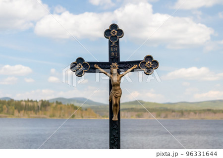 Crucifix - statue of Jesus Christ on a cross, in the background landscape with water, hills and blue sky with clouds Crucifix - statue of Jesus Christ on a cross, in the background landscape with water, hills and blue sky with clouds 96331644