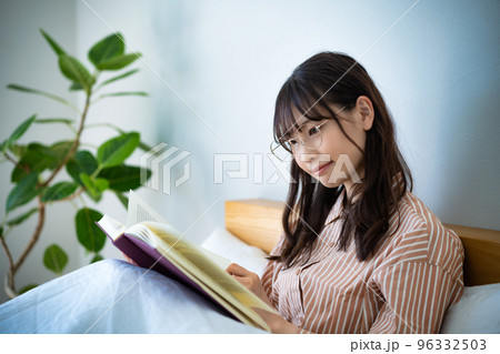 ベッドで読書する眼鏡の若い女性 96332503