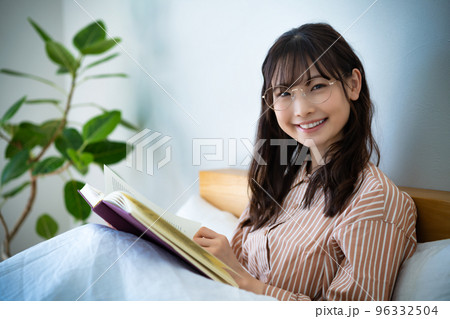 ベッドで読書する眼鏡の若い女性 96332504