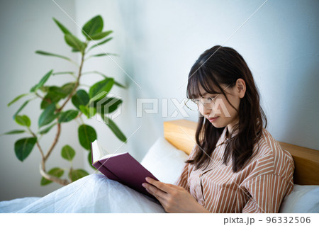 ベッドで読書する眼鏡の若い女性 96332506