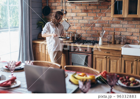 Young woman in the kitchen frying food in a frying pan Young woman in the kitchen frying food in a frying pan 96332883