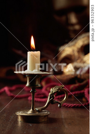 Burning candle in an old brass candlestick and carnival masks. 96332903
