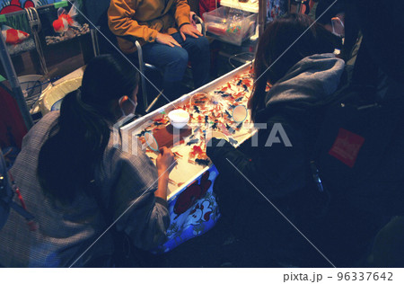 縁日の夜店の灯りに誘われ金魚すくいに挑戦、童心に帰って逃げる金魚を追う 96337642