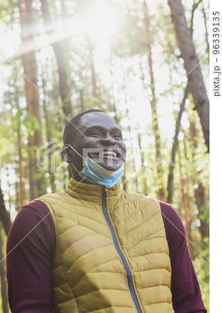 Handsome african american man wearing casual clothes and medical mask smiling happy walking in city park - end of pandemic 96339135