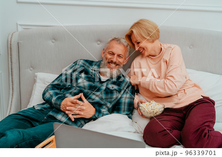 Husband and wife watch a film on the bed and eat popcorn 96339701
