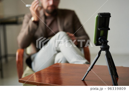 Close-up of of tripod with mobile phone standing on table while psychotherapist having video call 96339809