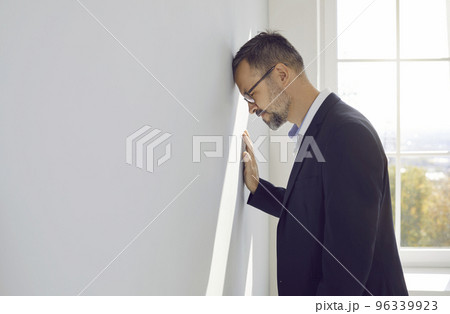 Businessman gets tired of problems, feels frustrated and bangs his head against office wall 96339923