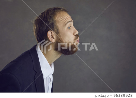 Profile view of a man with pursed lips waiting for a kiss while standing on a gray background. 96339928