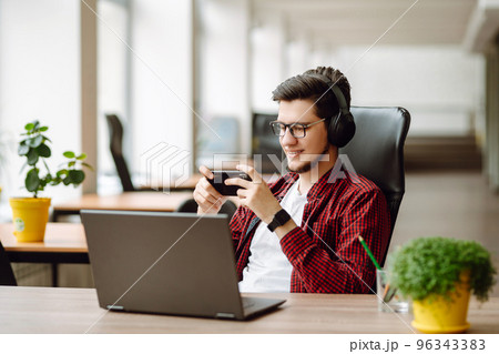 Creative man looking at screen typing message with smartphone. Young man relaxing using laptop. 96343383